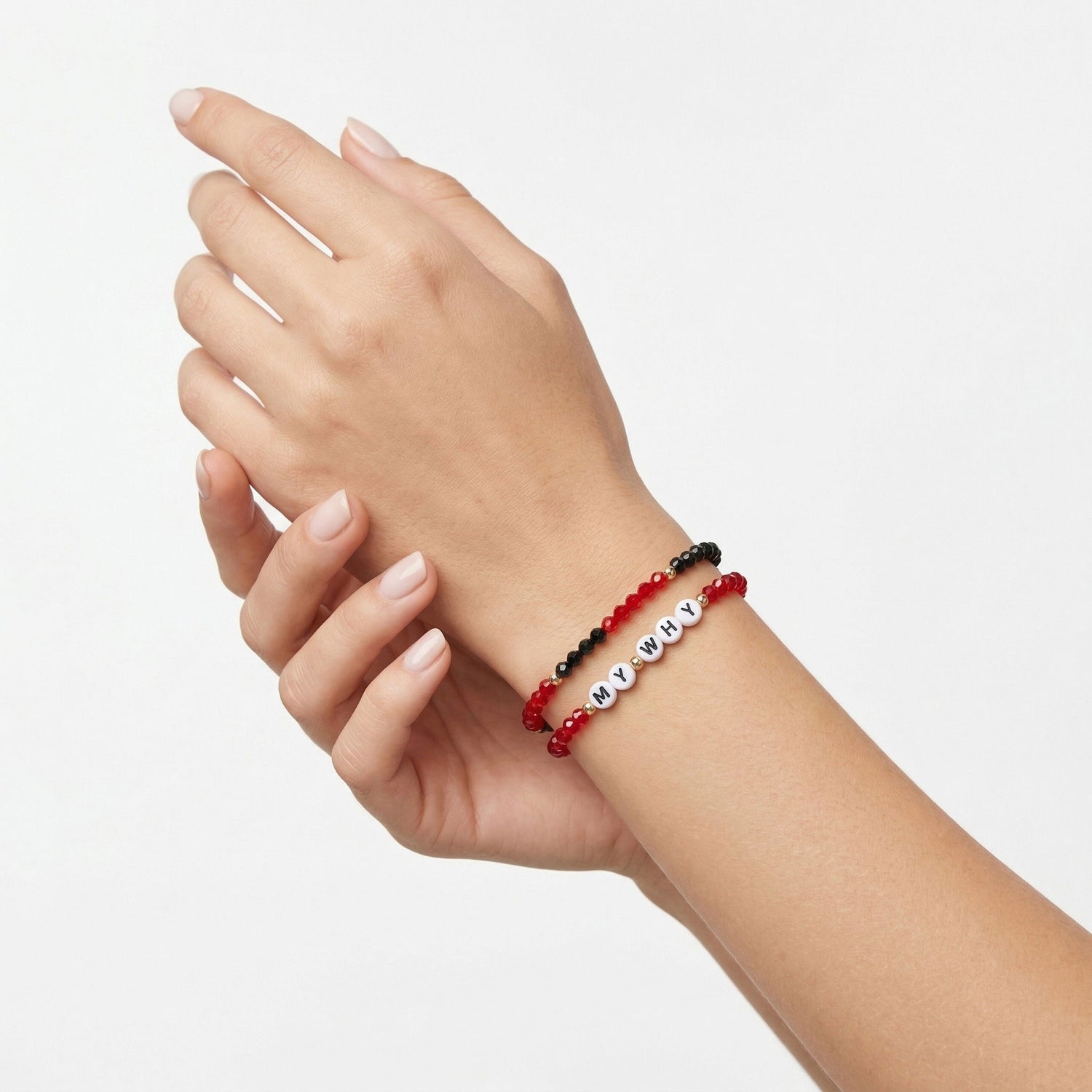 A close-up of a person's wrist wearing two beaded bracelets: one red and black, and one white with silver lettering spelling 'MY WHY'.