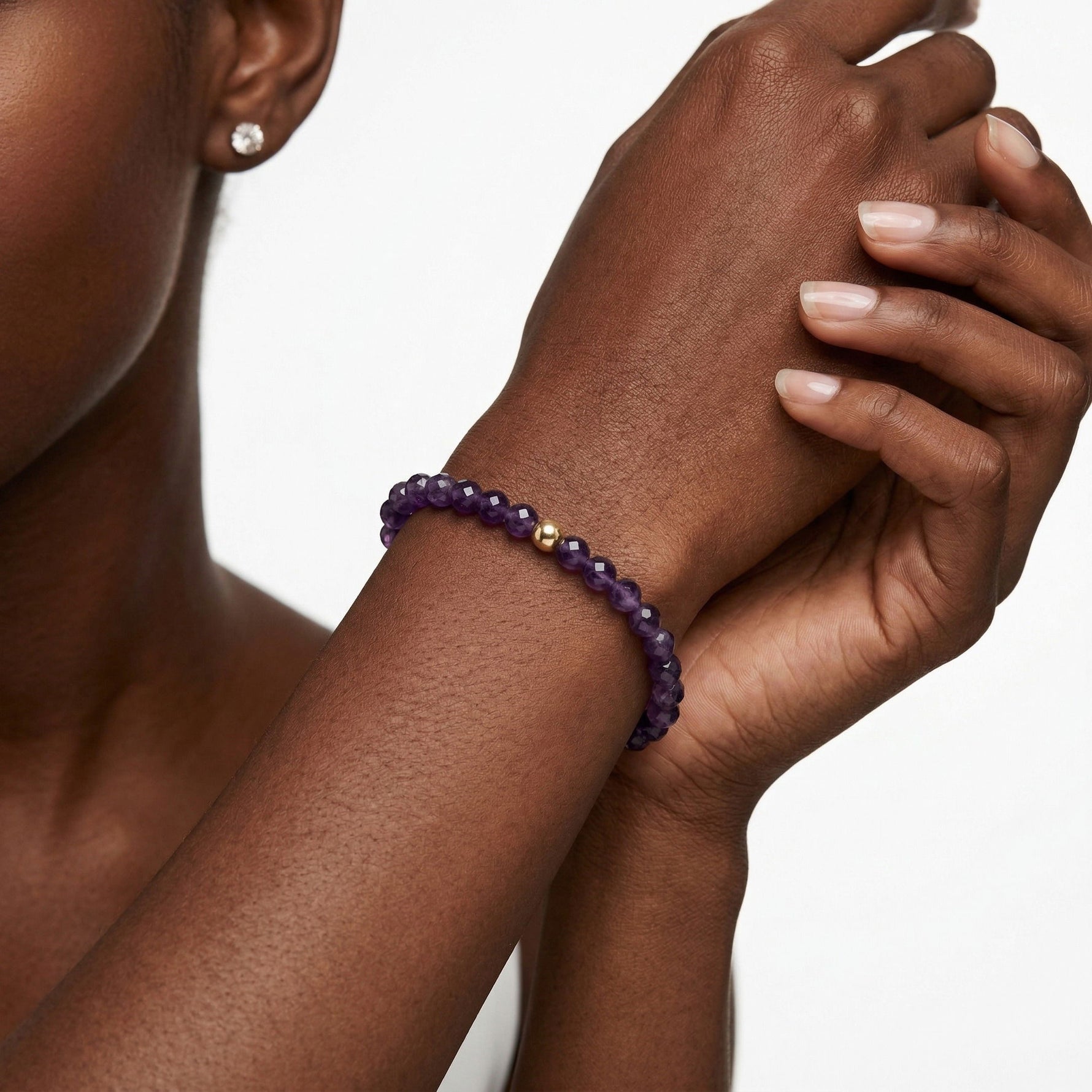 A close-up of a person's wrist wearing a purple beaded bracelet with a single gold accent bead, against a clean white background.